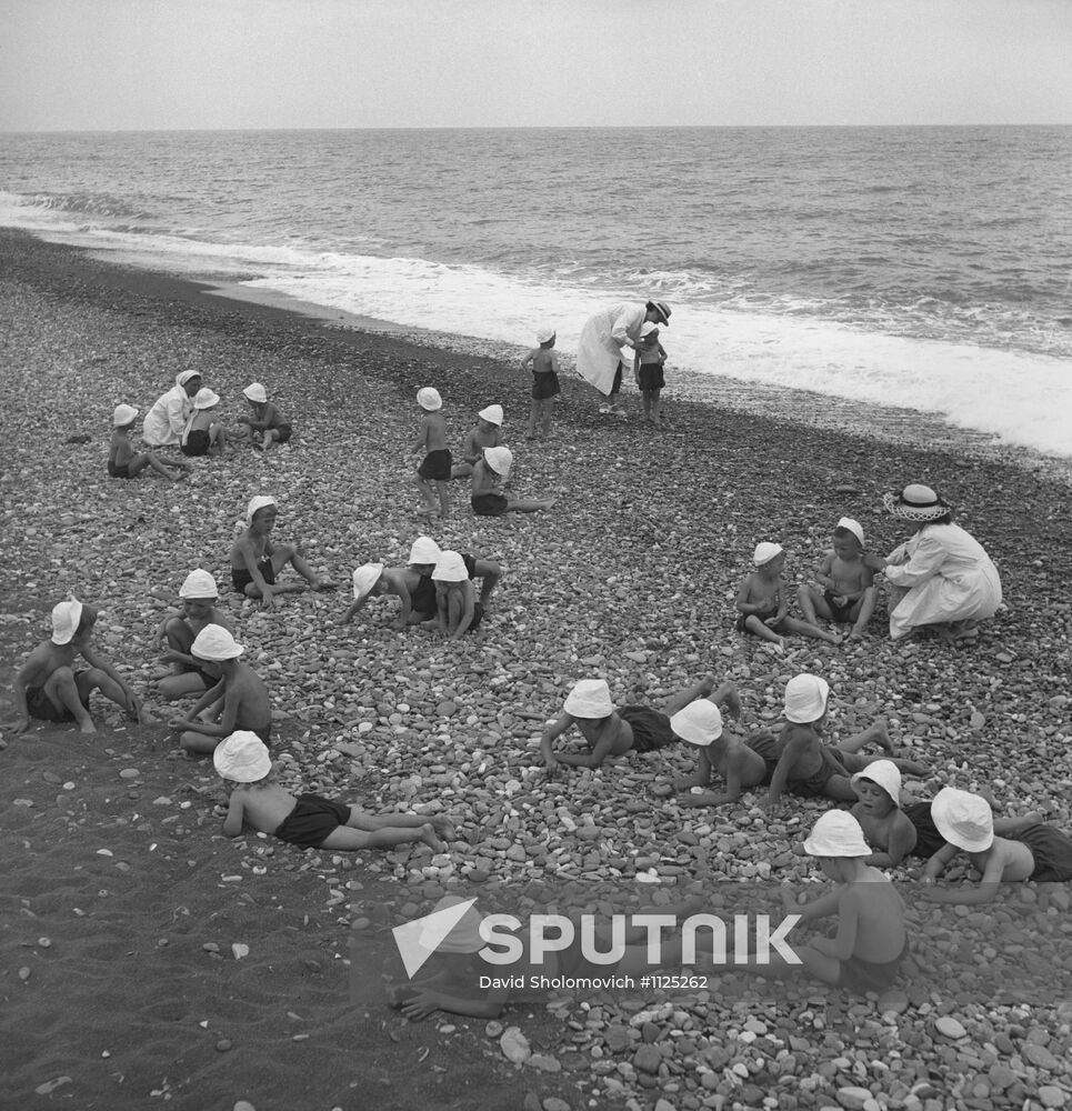 Children in charge of child-minders take rest on shore of Black Sea