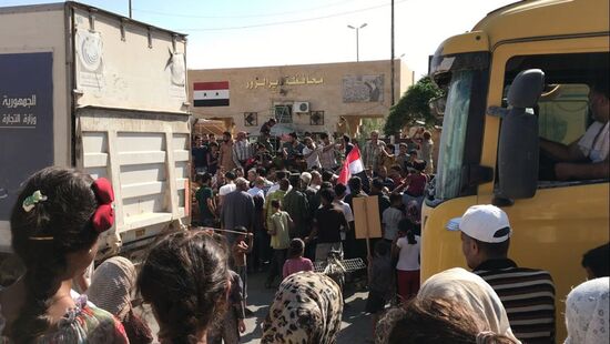 Deir ez-Zor residents welcome a truck convoy of medicines and food