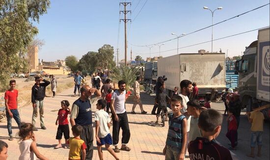 Deir ez-Zor residents welcome a truck convoy of medicines and food