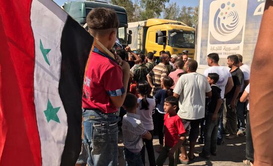 Deir ez-Zor residents welcome a truck convoy of medicines and food