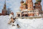 A woman poses for a photo as she sits in a snowbank with the Kremlin's Spasskaya Tower and Saint Basil's Cathedral seen in the background, in Moscow, Russia. Location: Russia, Moscow. Author: Sergey Pyatakov. Russia Winter