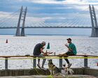 Young men have snacks while sitting on the guardrail of the the embankment at the Sevkabel Port in Saint Petersburg, Russia. The port used to be an industrial area that has reconstructed into a complex of art objects where residents spend their spare time. Location: Russia, Saint Petersburg. Author: Alexander Galperin/Sputnik. Russia Urban Landscaping